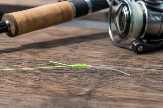 Finished FG knot joining bright braided line to a clear fluorocarbon leader beside a fishing rod and reel